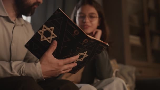 聖なるトーラーの本を持っている匿名のユダヤ人男性の手の閉じた選択的な焦点ショット デイビッドの星は カバーの上に 自宅でソファーに座って 十代の娘と聖書を議論しながら — ストック動画