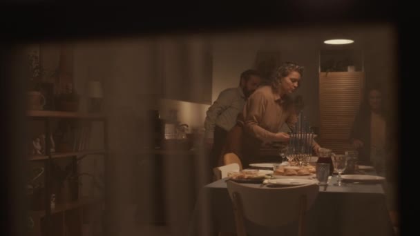 フルショット 窓のカーテンを介して ハヌカを祝うお祝いの夕食のための3つの層テーブルのユダヤ人の家族の 伝統的な料理を運ぶ ゲストを待っている間チャット — ストック動画