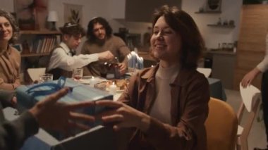 Genç Yahudi bir kadının küçük kız kardeşine hediye verirken ve Hanuka kutlamasında iyi şeyler dilerken aile üyeleri şenlik masasında oturup akşam yemeği hazırlarken orta boy bir fotoğraf.