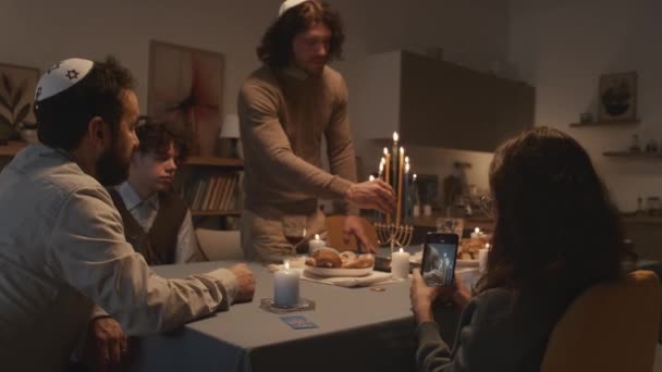 在基帕的中年犹太守寡男子和他的孩子们在家里庆祝光明节 大儿子在中东点燃蜡烛 小女儿在智能手机上拍照 — 图库视频影像