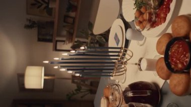 Geleneksel Yahudi ziyafeti için aile evinde hazırlanmış orta boy sofra resmi. Yanan mumlarla menorah, sütlü tabaklar, sufganiyot, humus, misafirleri bekleyen.