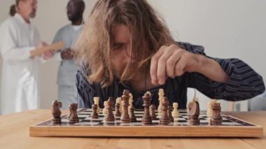 Şizofreni hastası beyaz bir adamın seçmeli odak portresi hastanede ortak odada satranç oynarken birden sinirleniyor.