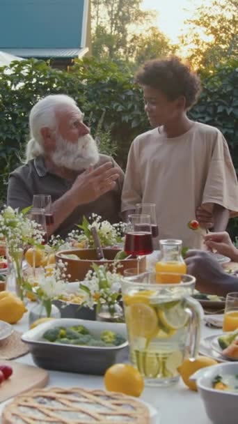 長髪のシニアの男の垂直ショットと彼の孫と話し 家族の夕食で彼を抱きしめました — ストック動画
