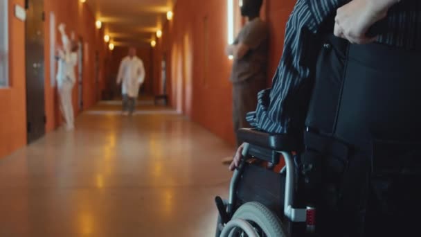 无法辨认的护士沿着精神病医院走廊带着病人坐轮椅到病房的选择性聚焦镜头 复制空间 — 图库视频影像