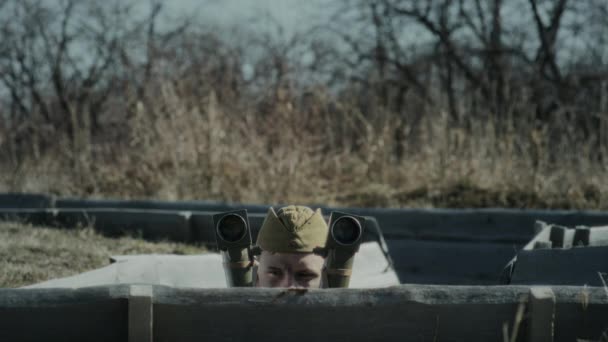 フォートラインのトレンチに立っている若いソビエト兵士は慎重に距離を調べ その後周辺の双眼鏡を使用して Word War 2の再現 — ストック動画