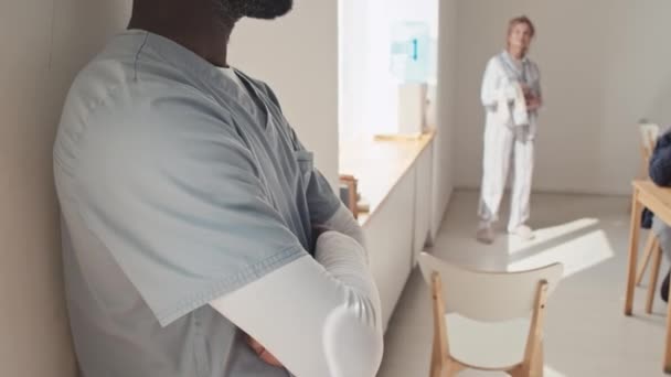 若いアフリカ系アメリカ人医師の選択的なフォーカスショットは 患者の世話をしながら腕を横切って立って精神病院で働いています — ストック動画
