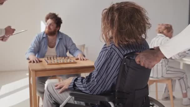 認知できない医療従事者が 精神障害のある男性を 仲間の患者に連れて行き チェスを始める — ストック動画
