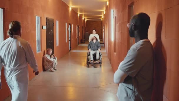 選択的なフォーカスショット アフリカ系アメリカ人の医療従事者が患者を診察する精神病院の廊下に立っている — ストック動画