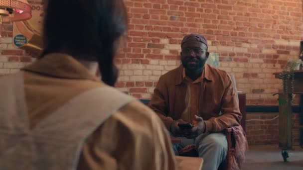 彼のガールフレンドの前で古い椅子に座っている若いアフリカ系アメリカ人の散歩の選択的な焦点オーバーショット — ストック動画