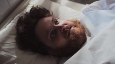 Deli gömleği giymiş sakallı bir adamın yüksek açılı portresi hastane yatağında nöbet geçiriyordu.