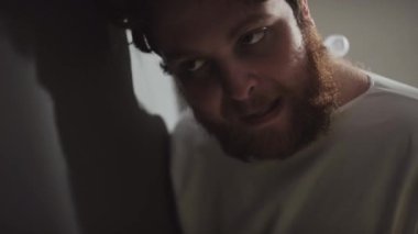 Zihinsel bozukluğu olan genç beyaz adamın yakın plan portresi. Kafasını gri duvara çarpıp arkasını dönüyor.