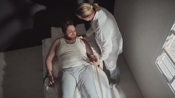 ベルトを使用して病院のベッドに統合失調症の積極的な患者を結ぶ精神保健クリニックで働く成熟した医者の上記のビューのショット — ストック動画