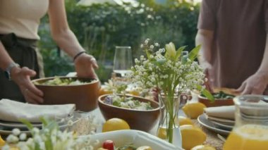 Yaşlı kadın ve kızının arka bahçede çiçeklerle ve limonlarla süslenmiş yemek masasını hazırlarken seçici bir odak noktası.
