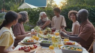 Modern etnik çeşitlilikte bir aile arka bahçede yemek yiyor, büyükbaba torunuyla konuşuyor ve sarılıyor.
