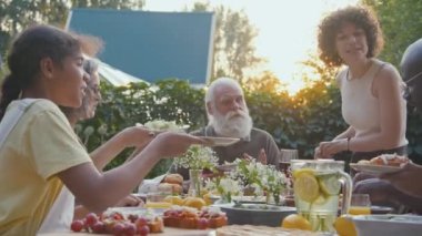 Neşeli beyaz kadın dışarıda aile yemeği yerken yemek masasında salata hazırlıyor.