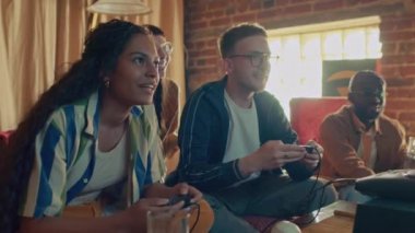 Etnik çeşitliliğe sahip bir grup arkadaş retro konsol oyunu oynamaktan zevk alıyor, beyaz adam kazanıyor.
