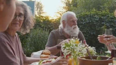 Kıdemli adam ve kadın yemek masasında oturup yemek yiyor ve aile üyeleriyle konuşuyor.
