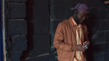 Sıradan kıyafetler giymiş, kişisel stereo çalar ve kulaklıklarla müzik dinleyen Afrikalı genç bir adamın orta boy portresi.