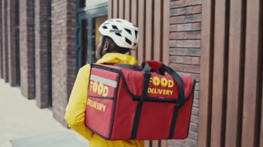 Erkek kuryenin şehir merkezindeki caddede yürürken çekilmiş orta ölçekli bir görüntüsü var.