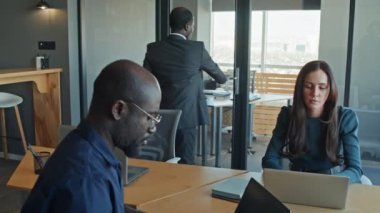 Siyahi erkek yönetmenin iş yerine gelip laptoplarda çalışan iki çok ırklı meslektaşın yanından geçerken orta derece yavaş çekimleri.