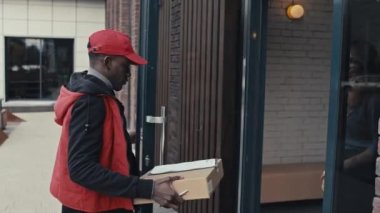 Teslimatçı adamın sarışın kadına paketi getirip kapıyı açarken ve belgeleri imzalarken PAN 'ın fotoğrafı.