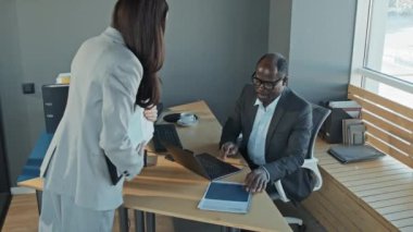 Yüksek açılı yavaş çekimde kadın çalışanın ofise girmesi ve incelenen bilgilere bakıp yeniden çalışması için geri vermesi için müdüre rapor vermesi.