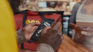 Lokanta çalışanına siparişi tarif eden kuryenin elindeki mobil uygulama ile cep telefonunun yakın çekimini yap