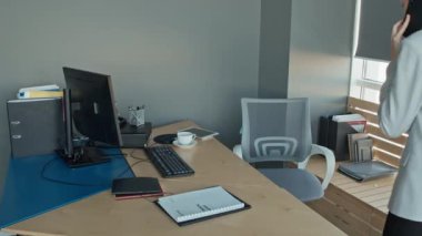 Beyaz kadın yönetmenin telefonda konuşurken, otururken, telefonu masaya koyarken, dizüstü bilgisayar açarken ve rapor alırken orta yavaş çekimleri.