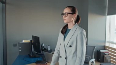 Kafkas iş kadınının gözlüklü orta yavaş portresi kameraya doğru dönüyor ve ofiste katlanmış kollarla poz veriyor.