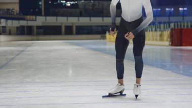 Genç çift ırklı sporcunun düşük pozisyonda çömeldiği ve kapalı buz pateni sahasında hızla koşarken orta yavaş bir bıçak darbesi.