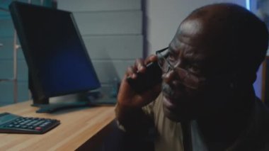 Siyah gözlüklü, tezgahın yanında saklanan ve muayene odasında telefonla konuşan siyahi bir adamın el kamerası görüntüsünü yakın çekim yapın.