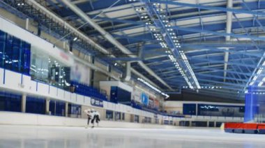 İki beyaz erkek hız patencisinin kapalı alandaki buz pateni pistinde antrenman yaparken ve yarışırken uzun ve yavaş bir çekim.