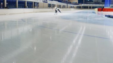 Profesyonel buz pateni takımı giymiş üç çok ırklı erkek buz pateni pistinde antrenman yaparken uzun ve yavaş çekim yapıyor.