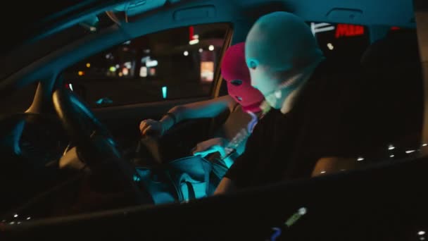 中侧手持照片的年轻白人男性罪犯身穿巴拉克拉瓦上车 晚上和女友坐在车里享受偷来的钱 — 图库视频影像