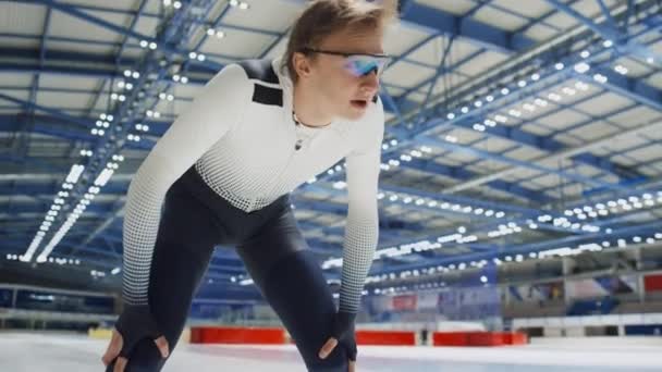 屋内アイスリンクでのトレーニング後にスピードスケートユニフォームで疲れた白人若い男性アスリートの低角度手渡されたショット — ストック動画