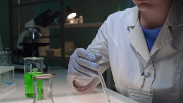 クローズアップタイルダウン 顔と義肢を持つ女性科学者の手 白いコートで細胞培養ソリューションを緑の基質でペトリ皿に落とし バイオテクノロジーラボで研究 — ストック動画