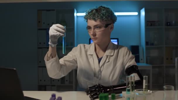 バイアルで化学溶液を準備する義肢を持つ若い女性ラボアシスタントのミディアムショットは ラップトップでタイプしている中年白人研究者にそれを与え 実験を行っている間 — ストック動画