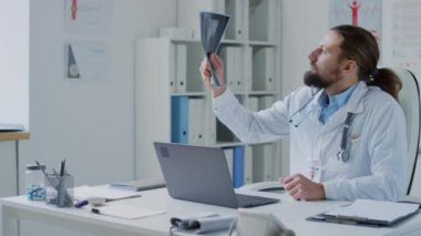 Beyaz bir erkek doktorun göğüs röntgenine bakarken orta boy fotoğrafı. Sonra da hastaneye laptoptan bilgi girişi.