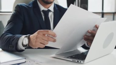 Orta ölçekli iyi görünümlü genç Orta Doğulu iş adamının çalışma saatleri boyunca hafif ofiste oturup belgeler okuması.