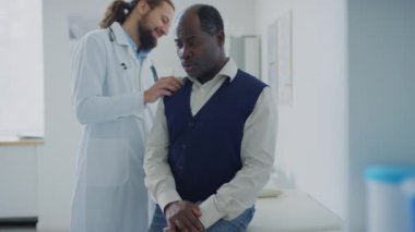 Kafkasyalı bir doktorun, özel klinikteki randevusu sırasında şikayetlerini anlatan Afrikalı Amerikalı bir hastayı muayene ederken orta ölçekli bir pozu.