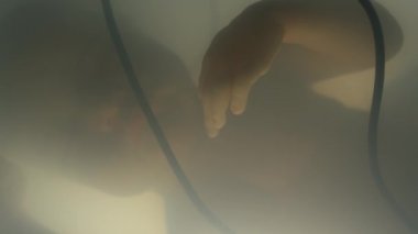 Laboratuvarda yüzen ve yapay rahmin içinde amniyotik sıvı üreten ve kablolarla beslenme sistemine bağlı uyuyan yetişkin bebek silueti.