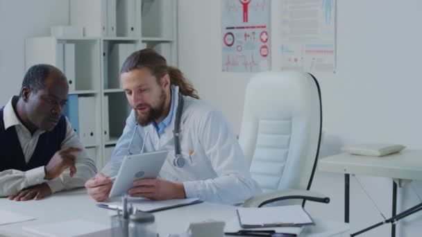 Średnie Ujęcie Kaukaskiego Lekarza Trzymającego Tabletkę Wyjaśniającego Schemat Leczenia Afroamerykańskiemu — Wideo stockowe