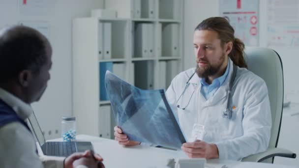 男性高加索放射专家在临床预约期间检查黑人病人时诊断脊柱的中盘摄影 — 图库视频影像