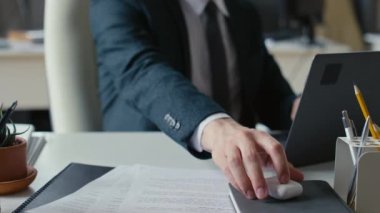 Ofiste çalışırken bilgisayarında yazı yazan ve kulaklıktan kablosuz kulaklık alan tanınmayan bir ofis çalışanının görüntüsü.