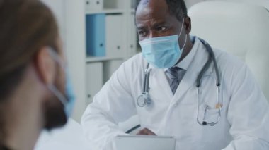 Hastanedeki randevusu sırasında elinde tablet olan Afrikalı Amerikalı pratisyen hekimin ve hastaların online sağlık geçmişine şikâyetlerini yazarken orta boy fotoğrafı.