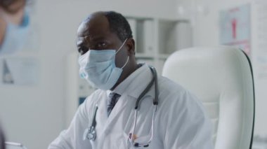 Siyahi erkek pratisyen hekimin semptomlar hakkında danışmanlık yaptığı ve sağlık kliniğindeki randevusu sırasında açıklama yaptığı orta ölçekli bir fotoğraf.