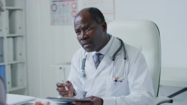 Afrika kökenli Amerikalı bir doktorun hastalarla sağlık sorunları ve doktor muayenehanesindeki sağlık geçmişine dair şikayetler yazarken orta boy fotoğraf çekimi.