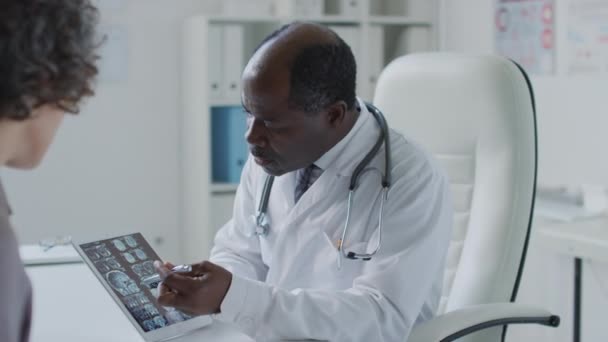 中侧拍摄黑人男性医生持片 并在诊所预约期间向女性病人解释断层扫描结果 — 图库视频影像
