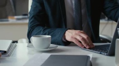 Tanınmayan iş adamının laptoptaki işini bitirip ofiste kahve molası verirken görüntüsü.