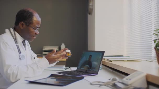 病気の患者に薬を処方し ラップトップ上のオンラインビデオ通話中にその使用を説明するアフリカ系アメリカ人医師の中側ショット — ストック動画